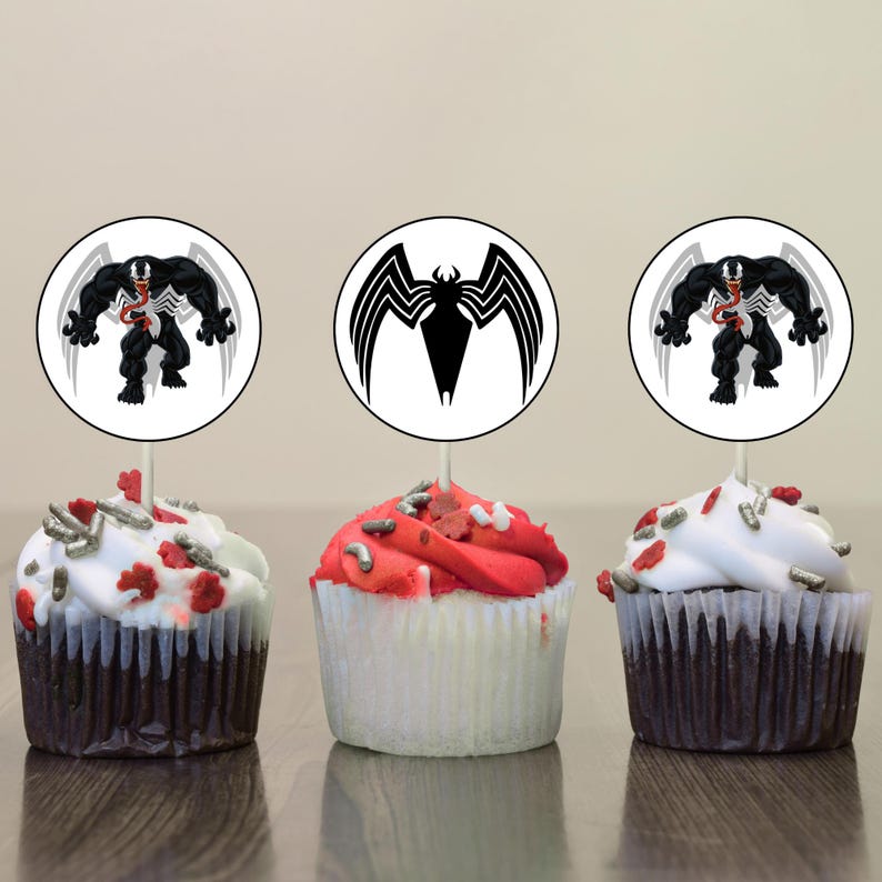 May include: Three cupcakes decorated with red and white frosting and topped with silver sprinkles. Each cupcake has a round, white paper topper with a black and white image of the superhero Venom.