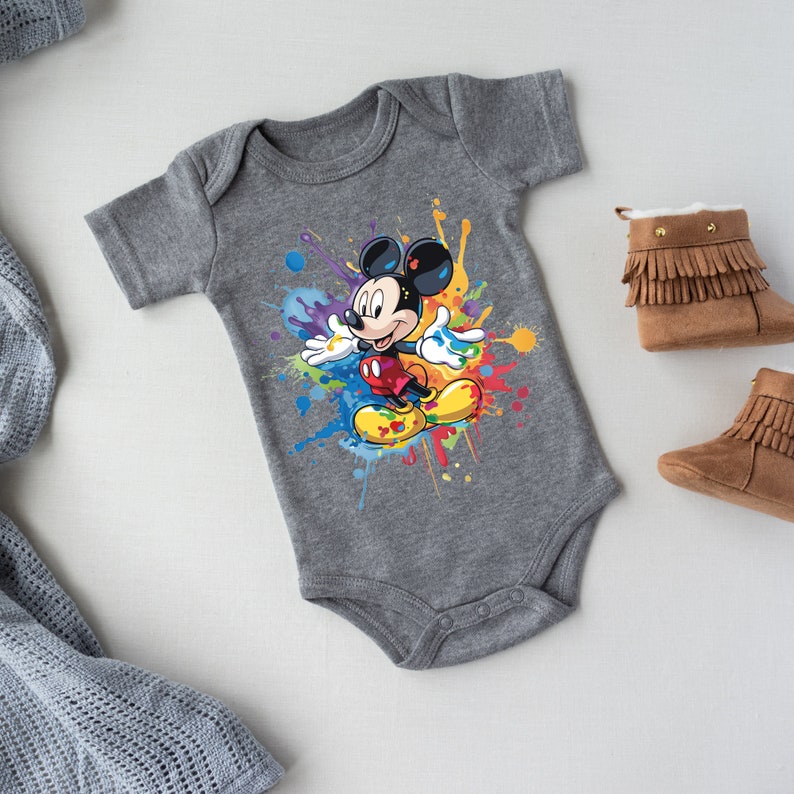 May include: A gray baby onesie with a colorful paint splatter design featuring Mickey Mouse in the center.