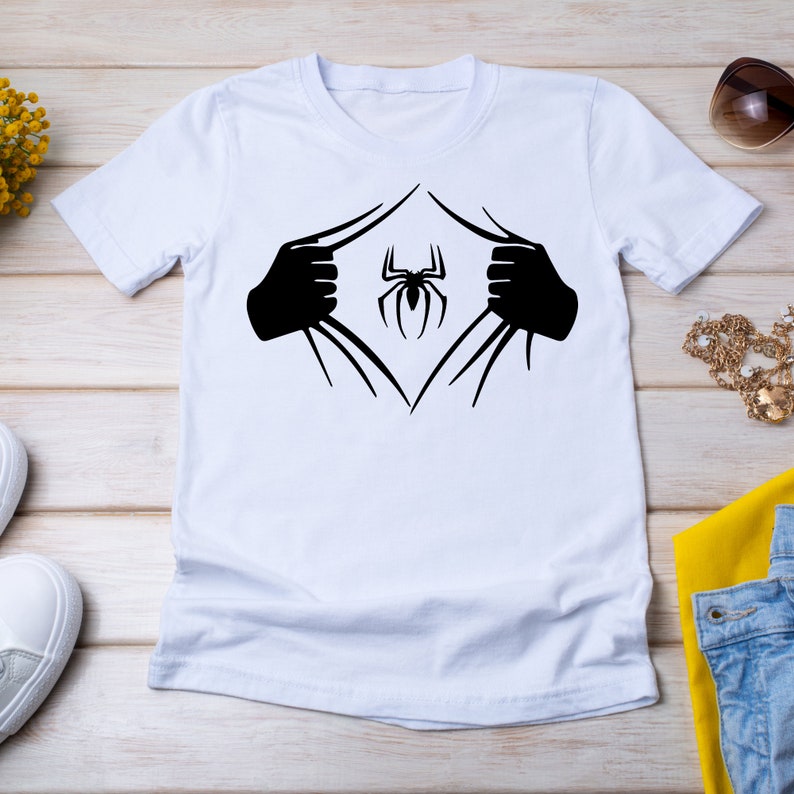 Puede incluir: Camiseta blanca con un gr&aacute;fico de ara&ntilde;a negra. La ara&ntilde;a parece estar emergiendo de la camiseta, como un superh&eacute;roe.