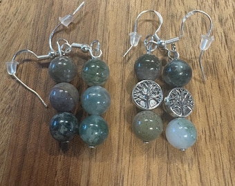 May include: A pair of handcrafted earrings with silver-tone hooks. Each earring features three round, green and gray beads. One earring has two silver-tone tree of life charms.