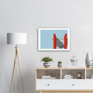 May include: A framed print of a minimalist illustration of a building with red accents against a light blue sky.