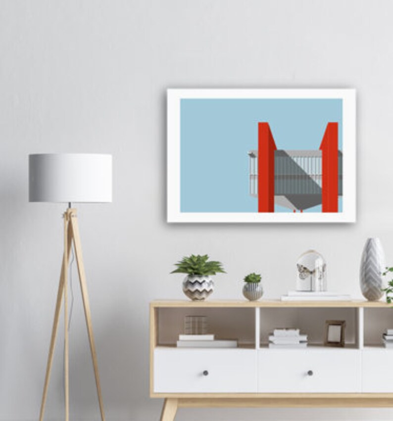 May include: A framed print of a minimalist illustration of a red building with a light blue sky background. The building has a geometric design with a flat roof and large windows. The print is displayed on a shelf with a lamp, plants, and other decorative items.