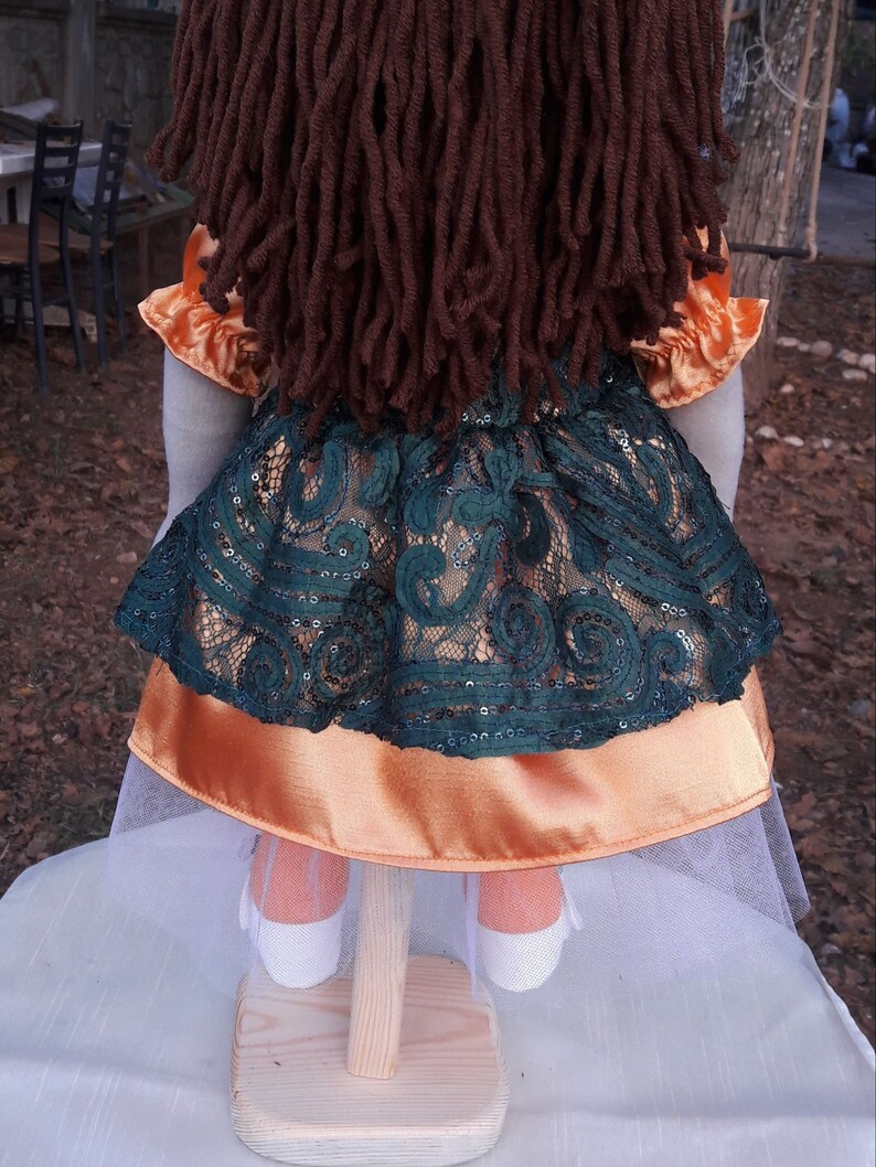 Puede incluir: Una mu&ntilde;eca hecha a mano con pelo largo de lana marr&oacute;n, que lleva un vestido de encaje verde con una falda interior de sat&eacute;n naranja y una falda de tul blanca.