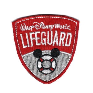 May include: A red and white embroidered patch with the words "Walt Disney World LIFEGUARD" in white lettering. The patch features a Mickey Mouse-themed life preserver in the center.