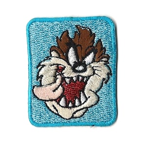 Könnte beinhalten: Ein blauer gestickter Aufnäher mit einer Karikatur des Tasmanian Devils mit weit offenem Mund und herausgestreckter Zunge.