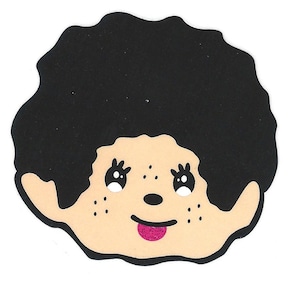 May include: A die-cut sticker featuring a cartoon face with black curly hair, light skin, and a pink tongue sticking out. The face has small freckles and white flower-shaped eyes.