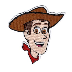 Puede incluir: Parche bordado con un personaje de dibujos animados de vaquero con sombrero marrón, pelo castaño y pañuelo rojo. El personaje tiene una expresión sonriente y ojos grandes y expresivos. El parche tiene un borde blanco.