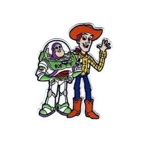 May include: Embroidered patch featuring the characters Woody and Buzz Lightyear from the animated film Toy Story. Woody is wearing a cowboy hat, yellow shirt, blue pants, and orange boots. Buzz Lightyear is in his signature spacesuit.