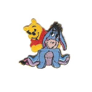 May include: Embroidered patch featuring Winnie the Pooh and Eeyore. Winnie the Pooh is yellow and wearing a red shirt. Eeyore is blue and has a sad expression.