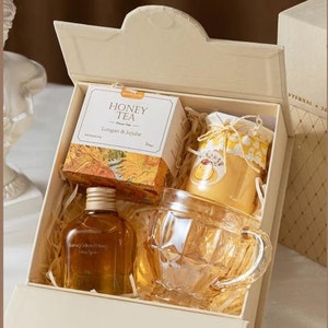 Puede incluir: Una caja de regalo blanca con la tapa abierta, que revela una taza de vidrio, una botella de miel y una caja de t&eacute; de miel. La caja de t&eacute; tiene las palabras "Honey Tea" y "Longan & Jujube" impresas en ella.