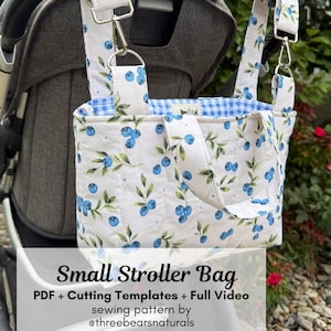 May include: A quilted stroller bag featuring a white fabric with a blue blueberry and green leaf print, blue and white gingham lining, and silver metal hardware. The text reads: Small Stroller Bag PDF + Cutting Templates + Full Video sewing pattern by @threebearsnaturals.