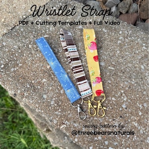 May include: Three fabric wristlet straps featuring a blue dandelion print, a brown and white striped pattern, and a yellow strawberry design. Each strap includes a metal swivel lobster clasp. Text reads: Wristlet Strap PDF + Cutting Templates + Full Video sewing pattern by @threebearsnaturals.