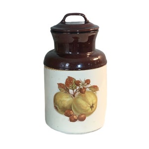 May include: A brown and white ceramic jar with a lid. The jar has a design of two green apples and a branch with leaves and nuts.