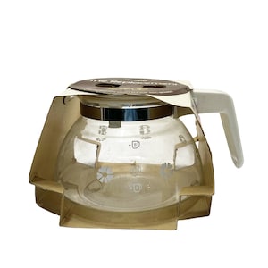 May include: A clear glass coffee pot with a white floral design and a silver lid. The pot is packaged in a brown box with the text "The Replacement Carafe" printed on it.