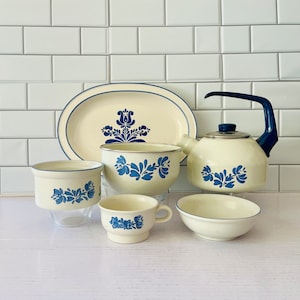 Puede incluir: Un juego de vajilla de cocina con estampado azul y blanco, que incluye una gran bandeja ovalada para servir, una tetera, un tazón para sopa, un tazón pequeño y una taza de té. Los platos presentan un diseño floral azul sobre fondo blanco.