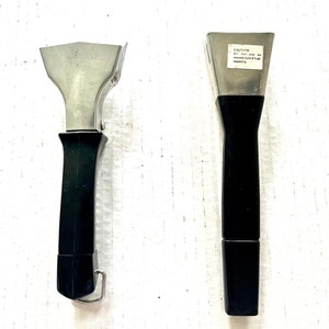 May include: Two black handled stainless steel pot holders. The smaller one has a hook on the end of the handle. The larger one has a warning label that reads "CAUTION: Do not use on vessels over 2/3 of capacity."