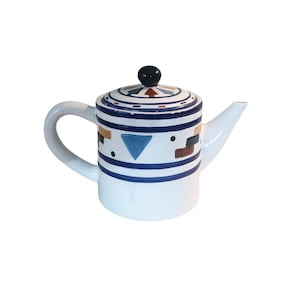 Puede incluir: Tetera de cerámica blanca con un patrón geométrico azul, rojo, amarillo y negro. La tetera tiene una tapa con un pomo negro.