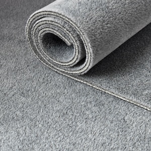 May include: A rolled-up, plush, gray rug with a soft, textured surface. The rug is partially unrolled, revealing the rolled interior and the edge with a contrasting border. The overall color is a muted gray.
