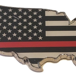 May include: A metal pin shaped like the United States of America with a thin red line across the middle of the American flag design. The flag is black and white with white stars on a black background.