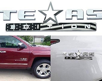 Könnte beinhalten: Silbernes Chrom-Emblem "TEXAS EDITION" mit einem Stern und einem amerikanischen Flaggenmuster. Das Emblem ist auf einem roten Pickup und einem weißen Pickup zu sehen.