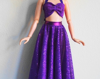 Peut inclure: Une poupée aux cheveux roux vifs et aux yeux bleus portant une tenue deux pièces composée d'un haut dos nu à sequins violets et d'une jupe longue assortie à sequins violets avec une ceinture métallique, debout en position verticale.