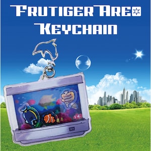 Könnte beinhalten: Ein durchsichtiger Acryl-Schlüsselanhänger mit einem Miniatur-Aquarium mit einem blau-gelben Fisch, einem orange-weißen Clownfisch und einer braun-weißen Muschel. Der Schlüsselanhänger ist an einem silbernen Delfin-Anhänger befestigt.