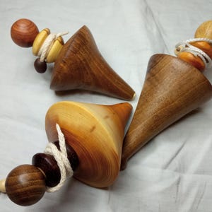 May include: Three wooden spinning tops with string and decorative beads. The tops are made of different types of wood, including a light brown wood, a dark brown wood, and a reddish brown wood.