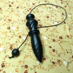 May include: A black wooden pendulum with a rounded top and a pointed bottom. The pendulum is attached to a black string with a small black ball at the end. The background is a floral pattern.