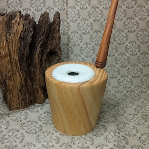 Könnte beinhalten: Eine Holzpfeife mit einem weißen Keramikkopf und einem Holzstiel. Die Pfeife liegt auf einer gemusterten Stoffoberfläche.