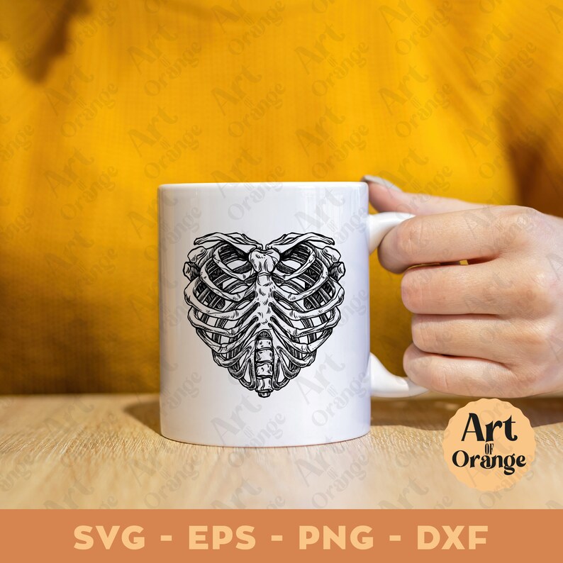 May include: White ceramic mug with a black and white illustration of a ribcage in the shape of a heart. The mug is on a wooden surface.