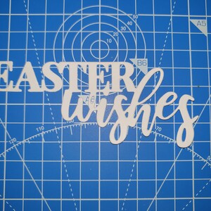 May include: White paper cut-out letters spelling "Easter wishes" on a blue cutting mat.