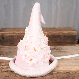 May include: A pink velvet witch hat with a pointed crown, adorned with white pearl beads and pink fabric flowers.