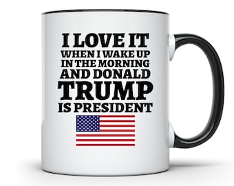 May include: White coffee mug with a black rim and handle. The mug has black text that reads "I LOVE IT WHEN I WAKE UP IN THE MORNING AND DONALD TRUMP IS PRESIDENT". An American flag is printed below the text.