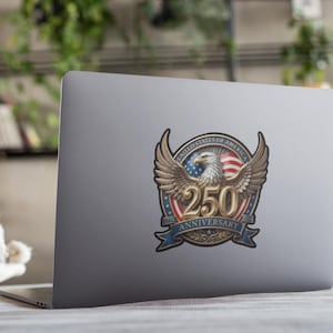 May include: A sticker on a laptop featuring a detailed emblem. The emblem includes a bald eagle with outstretched wings, the American flag, and the text "250 Anniversary" in a banner. The design is in shades of brown, red, white, and blue.