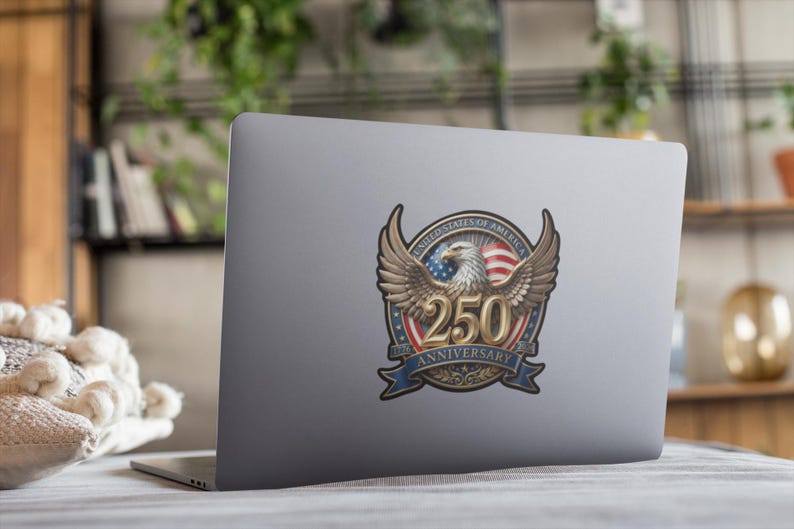 May include: A sticker on a laptop featuring a detailed emblem. The emblem includes a bald eagle with outstretched wings, the American flag, and the text "250 Anniversary" in a banner. The design is in shades of brown, red, white, and blue.