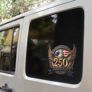 May include: A commemorative decal on a vehicle window. The decal features a golden eagle with outstretched wings, the American flag, and the text "250 Anniversary" in gold. The design is set against a black window.