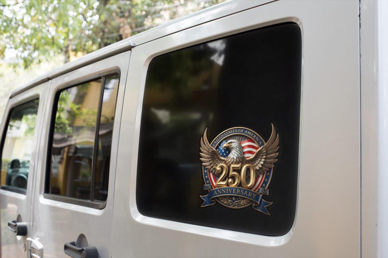 May include: A commemorative decal on a vehicle window. The decal features a golden eagle with outstretched wings, the American flag, and the text "250 Anniversary" in gold. The design is set against a black window.