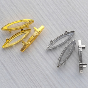 Op de afbeelding: Vier gouden en drie zilveren metalen instellingen voor het bevestigen van strasssteentjes of andere versieringen. De instellingen zijn ovaalvormig met een gat in het midden.