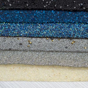 May include: Close-up of five rows of sparkly fabric, each row a different colour: black, blue, teal, silver, and cream.