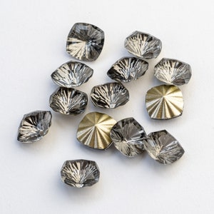 May include: A collection of 12 black and gold decorative embellishments. The embellishments are shaped like a flower with a pointed center. Some of the embellishments are clear and others are gold.