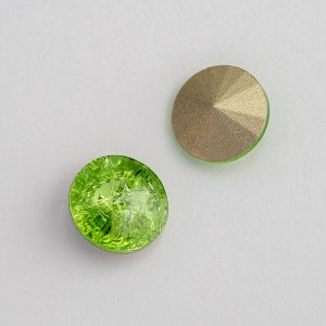 May include: Two round, green glass rhinestones. One rhinestone has a textured, iridescent surface. The other rhinestone has a smooth, metallic gold surface.