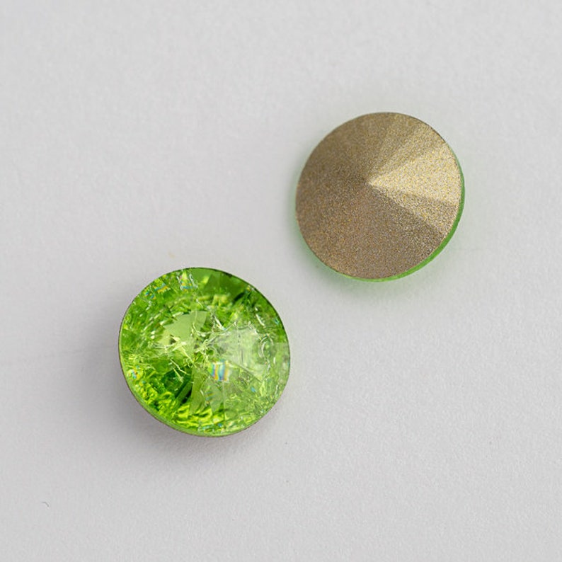 May include: Two round, green glass rhinestones. One rhinestone has a textured, iridescent surface. The other rhinestone has a smooth, metallic gold surface.
