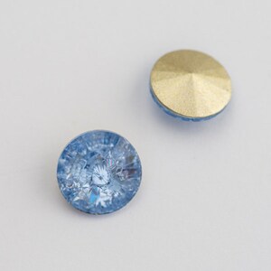 May include: Two round, light blue glass buttons with a gold metal backing. The buttons have a faceted design.