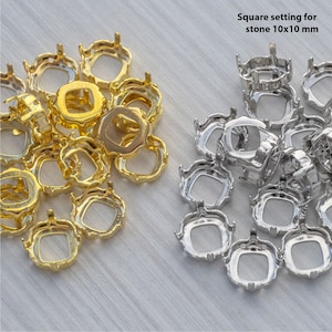 以下が含まれることがあります： 正方形の宝石用の金属製セッティングが2つの山になって写っているクローズアップ。セッティングは10mm×10mmで、ゴールドとシルバーがあります。