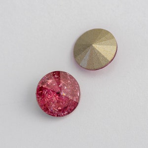 May include: Two round, flat-backed rhinestones. One is a clear gold color and the other is a deep pink with a glittery finish.