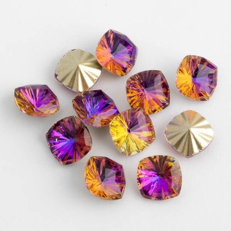 May include: Assortment of square-shaped iridescent glass rhinestones in shades of purple, orange, and yellow. The rhinestones have a faceted design and a shiny finish.