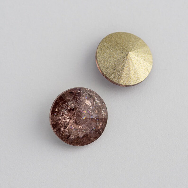 May include: Two round, flat-backed rhinestones. One is a light gold color and the other is a dark brown with iridescent shimmer.
