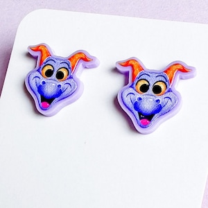 May include: A pair of purple and orange dragon earrings. The dragon has a friendly face with big eyes and a wide smile.