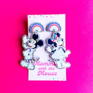 May include: A pair of novelty earrings featuring Mickey and Minnie Mouse designs. Each earring has a rainbow arch and a glittery outline. The earrings are on a white card with the text "Mommy with the Mouse" on a bright pink background.