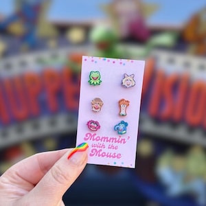 Könnte beinhalten: Eine rosa Karte mit sechs Ohrsteckern in Form von Charakteren. Die Ohrringe sind farbenfroh und zeigen verschiedene Charaktere. Auf der Karte steht der Text "Mommin' with the Mouse". Der Hintergrund ist unscharf.